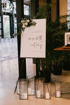 a sign that is sitting in the middle of a floor next to some plants and candles