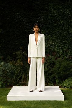 a woman standing on top of a white platform in front of some bushes and trees