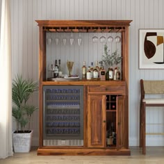 a wooden cabinet with wine glasses and bottles on it next to a chair in a room