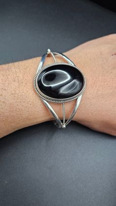 Check out this awesome sterling silver cuff bracelet featuring a big oval black onyx concho, measuring 30mm x 40mm! The bracelet is 43mm wide at its widest part, tapering down to 8mm, with a total length of 6 inches and a gap of 1-1 1/4 inches, perfect for wrists sized 7 to 7 1/2 inches. Made entirely from sterling silver right here in the USA, this bracelet is super cool! Now, let's talk about black onyx: It's a smooth, shiny black stone that's been loved by people for ages. Did you know it's o Black Polished Cuff Bracelet For Formal Occasions, Formal Black Cuff Bracelet With Polished Finish, Formal Black Polished Cuff Bracelet, Silver Oval Cuff Bracelet, Adjustable Black Cuff Bracelet With Polished Finish, Oval Cuff Bracelet With Polished Finish, Cozy Jewelry, Sterling Silver Cuff Bracelet, Let's Talk About