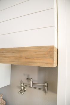 a wooden shelf above a sink in a white kitchen with stainless steel faucets