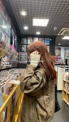 a woman in a store looking at cds on the shelf and talking on her cell phone