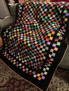 a black and multicolored quilt sitting on top of a couch next to a chair