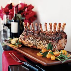 a large piece of meat on a wooden platter with oranges and flowers in the background