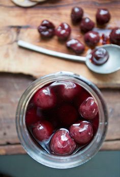 some cherries are in a jar on a wooden table with spoons next to it