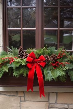 a window box with pine cones, holly and red ribbon tied around the bow on it