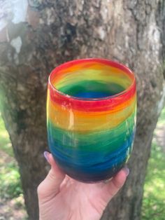 a hand holding a colorful glass in front of a tree