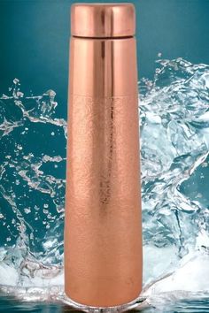 a copper colored water bottle floating on top of blue water with splashing around it