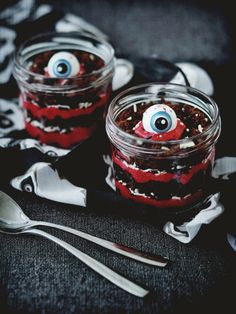 two mason jars filled with red and black cake topped with googly eyes, silverware