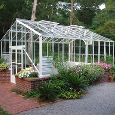 a small white greenhouse in the middle of some flowers and greenery on a brick walkway