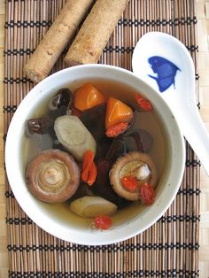 a bowl of soup with carrots, mushrooms and other vegetables next to a spoon