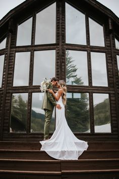 a bride and groom standing on steps in front of a large window with their arms around each other