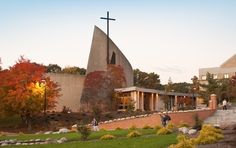 people are walking in front of a church with a cross on the roof and stairs leading up to it