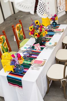 a long table set up with place settings and colorful flowers in vases on top