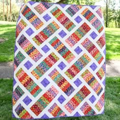 a colorful quilt hanging on the side of a tree in front of some green grass