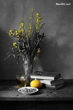 a vase with yellow flowers sitting on top of a table next to books and a plate