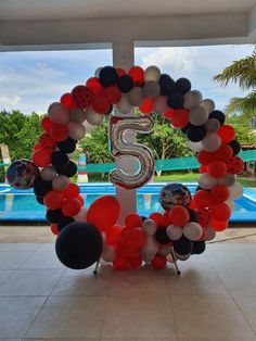 the number five balloon arch is decorated with red, white and black balloons in front of a swimming pool