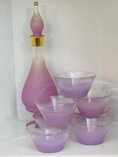 purple glass bowls are stacked next to a pink vase