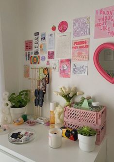 a white desk topped with lots of clutter and flowers next to a window covered in pictures