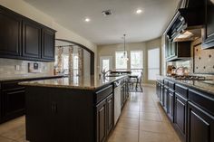 a large kitchen with black cabinets and marble counter tops, along with an island in the middle