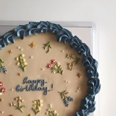 a birthday cake is decorated with flowers and the words happy birthday written in blue frosting