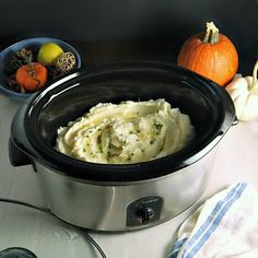 a crock pot filled with mashed potatoes on top of a table next to other food