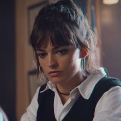 a woman in white shirt and black vest looking at camera