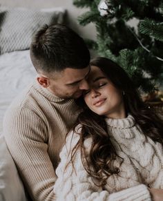 a man and woman cuddle in front of a christmas tree while holding each other