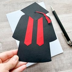 a hand holding a piece of paper with a red tie on it