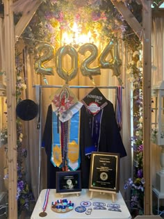 a table topped with trophies and plaques next to a wooden archway covered in balloons, streamers and flowers