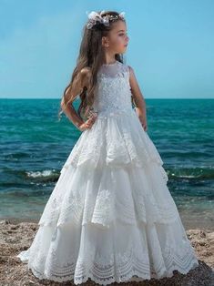 Say YES to this stunning girls' ball gown for Communion Day! Your lil' empress will adore the full,  tiered lace skirt ending in a beautiful train, and sheer bodice covered with enchanting flowers in front and back. Give her the dress of her dreams today! She can move and play confidently even after formal events and i Dressy Gowns, Girls Ball Gown, Special Occasion Gowns, Princess Flower Girl Dresses, First Communion Dress, Girls Couture, White Flower Girl Dresses, First Communion Dresses, Tiered Maxi Skirt