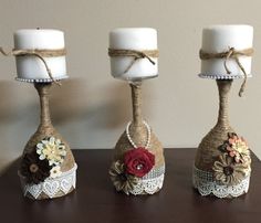 three white candles sitting on top of a wooden table next to two small vases