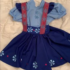 a blue dress with red trims and flowers on the back, sitting on a bed