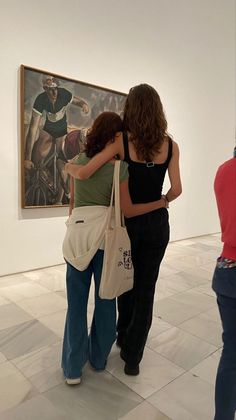 two women are hugging each other in an art gallery with paintings on the wall behind them