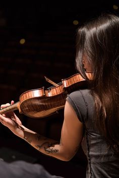 a woman holding a violin in her right hand and looking down at the strings on her left arm