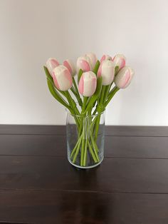 a glass vase filled with pink and white flowers on top of a wooden table next to a wall