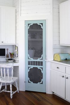 a kitchen with white cupboards and blue glass door in the center, next to a computer desk