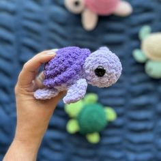 a hand holding a small crocheted turtle toy in front of other stuffed animals