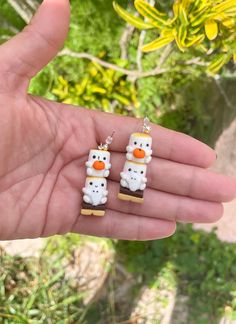 someone is holding out their hand with two small snowman earrings on it's fingers