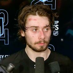 a man with long hair and beard standing in front of microphones, looking at the camera