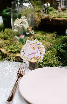 the table is set with pink plates, silverware and glass jars filled with flowers