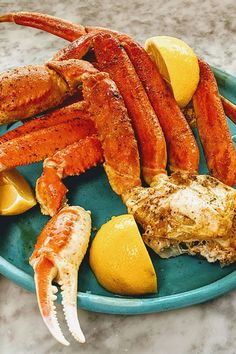 a blue plate with crab legs, lemons and other food items on top of it