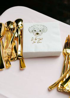 a napkin with a dog on it next to gold forks and knives