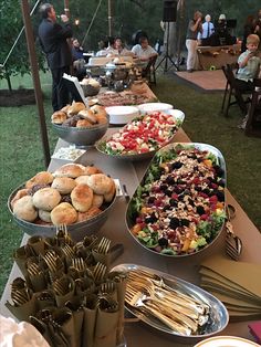 a long table filled with lots of food on top of a grass covered field next to people