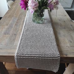 a vase filled with purple flowers sitting on top of a wooden table next to a white knitted runner