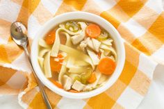 a bowl of chicken noodle soup on a checkered tablecloth