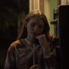 a woman talking on the phone while standing next to a telephone