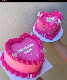 two heart shaped birthday cakes with pink frosting and butterflies on the top are being held by someone's hand