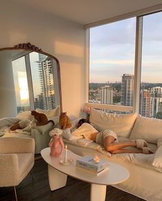 a woman laying on a couch in front of a large window next to a dog