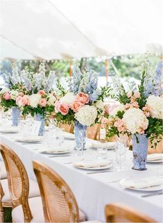 the table is set with white and pink flowers in blue vases on each side